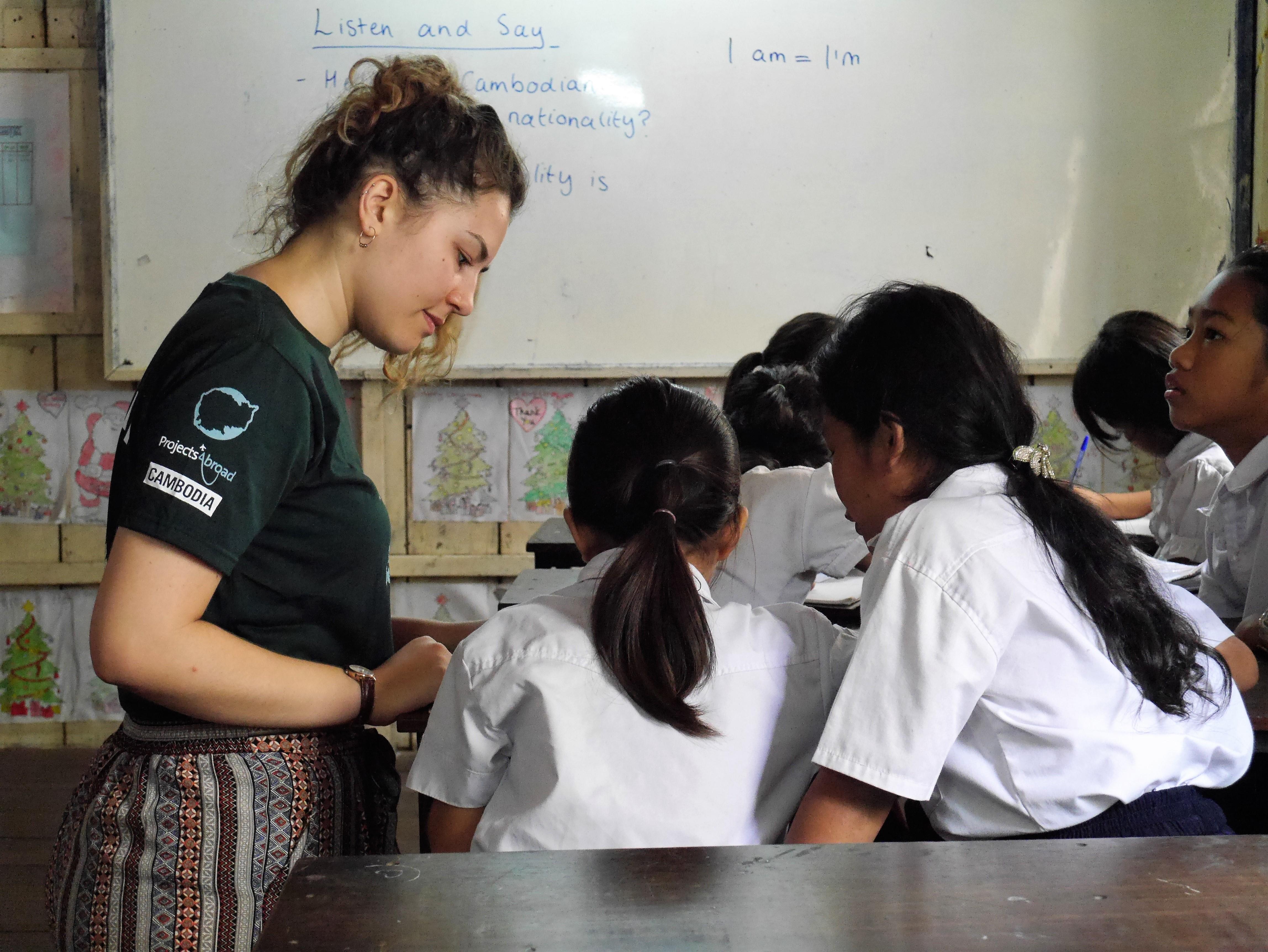 Projects Abroad volunteer helps two of her students during class as part of her teaching work experience in Cambodia Two students receive class work assistance from a volunteer teaching English in Cambodia